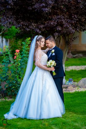 Wedding couple poses on manicured lawn with purple-leafed trees in the background.