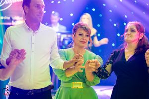 Guests dancing in formal attire under purple lighting at a wedding reception.