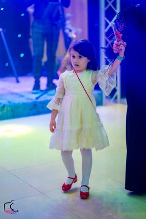 Young girl in white dress and red shoes dances under blue stage lighting.