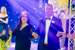 Couple dancing at formal event with blue and yellow lighting effects in background.