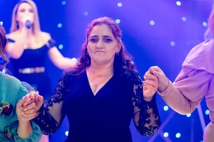 Woman in black dress dances with others at formal event under blue spotlights.