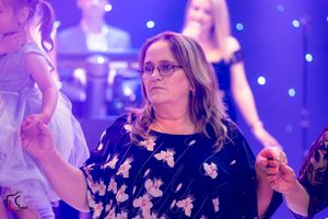 Woman in floral dress dances at formal event with purple and blue lighting.