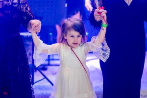 Young girl in white dress joyfully dances with arms raised under blue lighting.