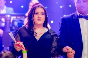 Woman in black dress dances at formal event with purple stage lighting.