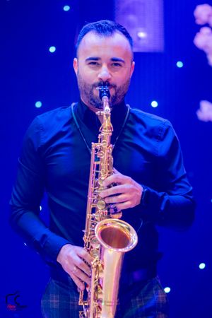 Musician playing saxophone on stage with dramatic blue lighting and starry backdrop.