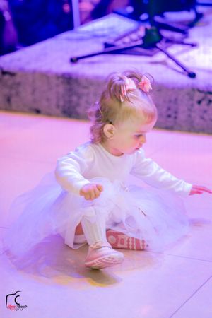 Small child in white dress crawling on illuminated dance floor with purple lighting.