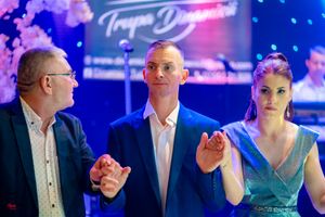 Formal event scene with people gathered under theatrical lighting and a branded backdrop.
