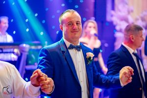 Formal event with attendees in suits and bow ties under vibrant blue lighting.