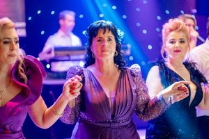 Lively dance party scene with guests in formal attire under purple and blue lighting.