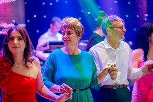 Guests in colorful formal attire dancing at an event with atmospheric blue lighting.