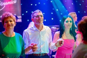 Party scene with people in vibrant outfits dancing under blue and pink spotlights.