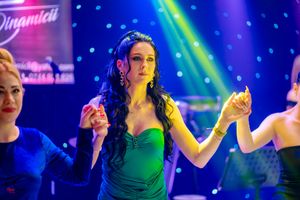 Woman in emerald green dress dancing gracefully under colorful stage lighting.