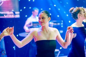 Elegant dancer in strapless black dress performing under blue stage lighting.
