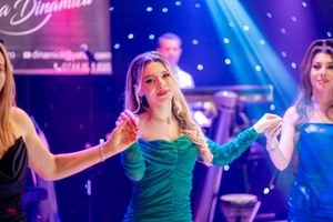 Dancers in elegant gowns perform synchronized movements under vibrant purple and blue stage lighting.