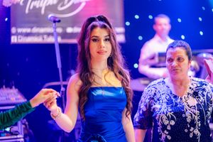 Dancers in formal evening wear perform under blue stage lights with live band in background.