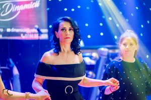 Performers in elegant black dresses dance under blue stage lighting at formal event.