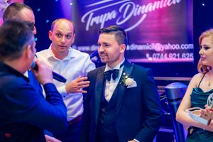 Formal event guests engaged in conversation under purple lighting with Trupa Dinamica signage visible.