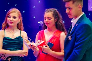 People in formal wear gathered at a celebration with decorative lighting and sparkly backdrop.