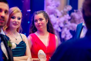 Formal event attendees gathered under purple lighting with floral decorations in the background.