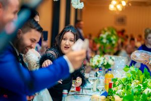 Wedding reception table decorated with bright green floral centerpieces and glowing chandeliers.