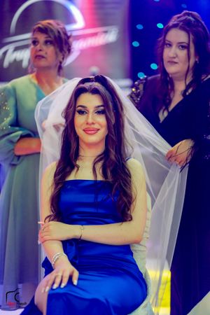 A bride in a blue dress and veil smiles during her wedding preparation.