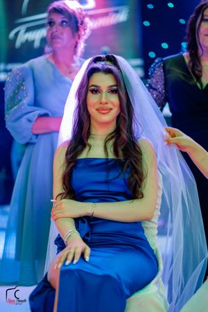 A bride wearing a royal blue dress and white veil poses under dramatic lighting.