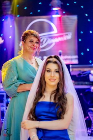 A bride in a sparkling white dress shares a tender moment with a guest in a turquoise gown at a wedding reception.