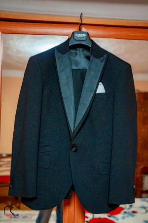 Three black formal suits hanging on display hangers against an orange wall.