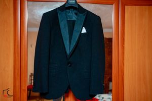 Row of black formal suits displayed on hangers in warm lighting.