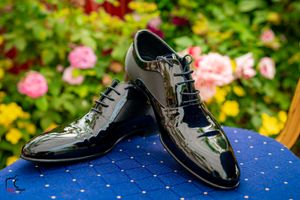 Shiny black formal dress shoes displayed on blue polka dot surface with garden background.