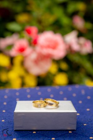 Two gold wedding rings displayed on a white surface against a blue polka dot background with pink flowers in bokeh.