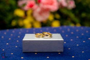 Wedding rings placed on white surface with colorful floral background and blue polka dot pattern.