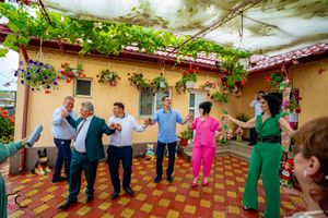 Festive outdoor celebration with dancers on checkered patio under vine-covered pergola.