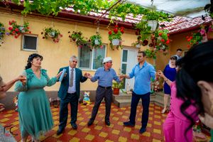 Wedding party dancing in formation on outdoor terrace with yellow walls and flowering vines.