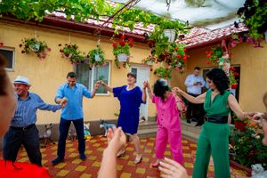Wedding party guests dance and celebrate on a colorful tiled patio with hanging flowers and red roof.