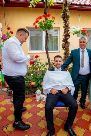 Formal event attendees interact on a patterned outdoor patio with floral decorations.