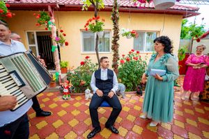 Festive outdoor gathering with musicians and guests on a decorated terrace with red flowers.