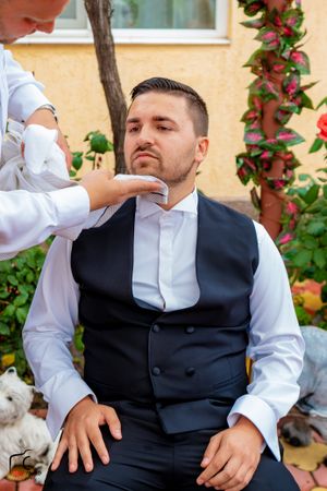 Person in formal attire sitting on patio with flowering vines and red roses in background.