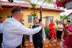 Wedding guests gather in a garden courtyard decorated with red flowers and a tiled roof.