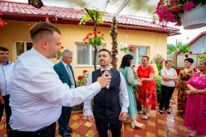 Guests celebrate at an outdoor wedding reception with vibrant floral decorations and a yellow building backdrop.