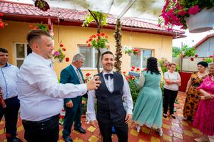 Festive outdoor wedding reception with guests in formal wear surrounded by blooming red flowers.