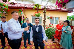 Wedding party members socialize at an outdoor venue adorned with red flowers and greenery.