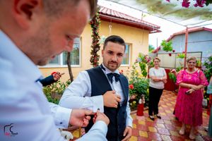 Outdoor wedding celebration with formal-dressed guests near blooming garden and yellow building.