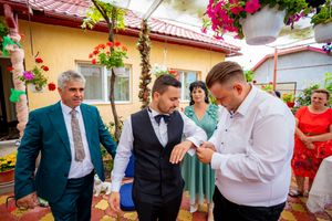 Wedding guests gather in a colorful courtyard decorated with hanging flowers and a red tiled roof.