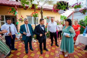 Garden party with formal attire against backdrop of yellow walls and hanging flower baskets.