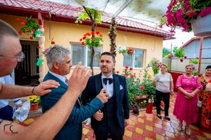 A group of people gather outside a yellow house decorated with hanging flower baskets.
