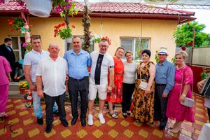 Celebratory gathering outside a yellow house with hanging flower baskets and decorative pavement.