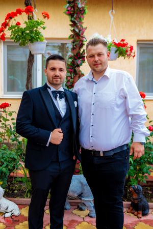 Men in formal attire pose together on decorative tiles with red flowers in background.