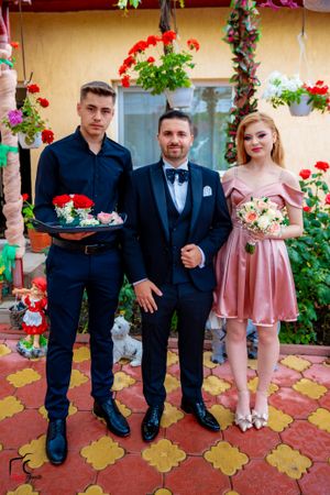 A group in formal attire poses together on a patio with red flowers and decorative tiles.