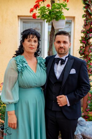 A formal portrait of two people against a yellow wall with red flowering plants and garden decor.